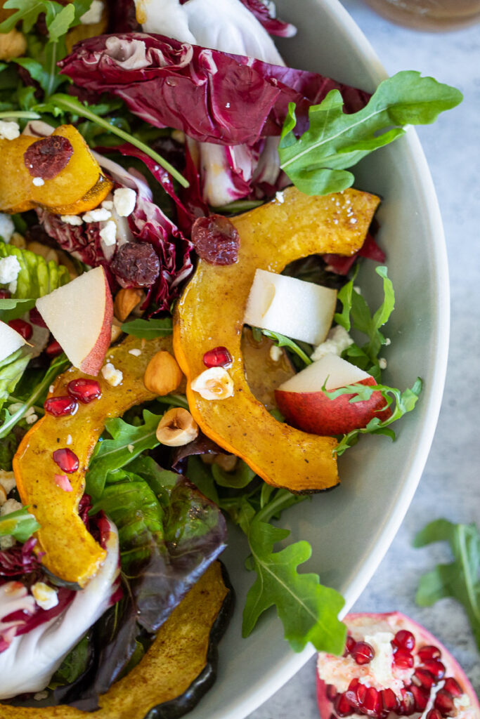 A bright Autuman Roasted Acorn Squash Salad with Maple-Spiced Vinaigrette boasting vivid colors of orange, reds and greens. 