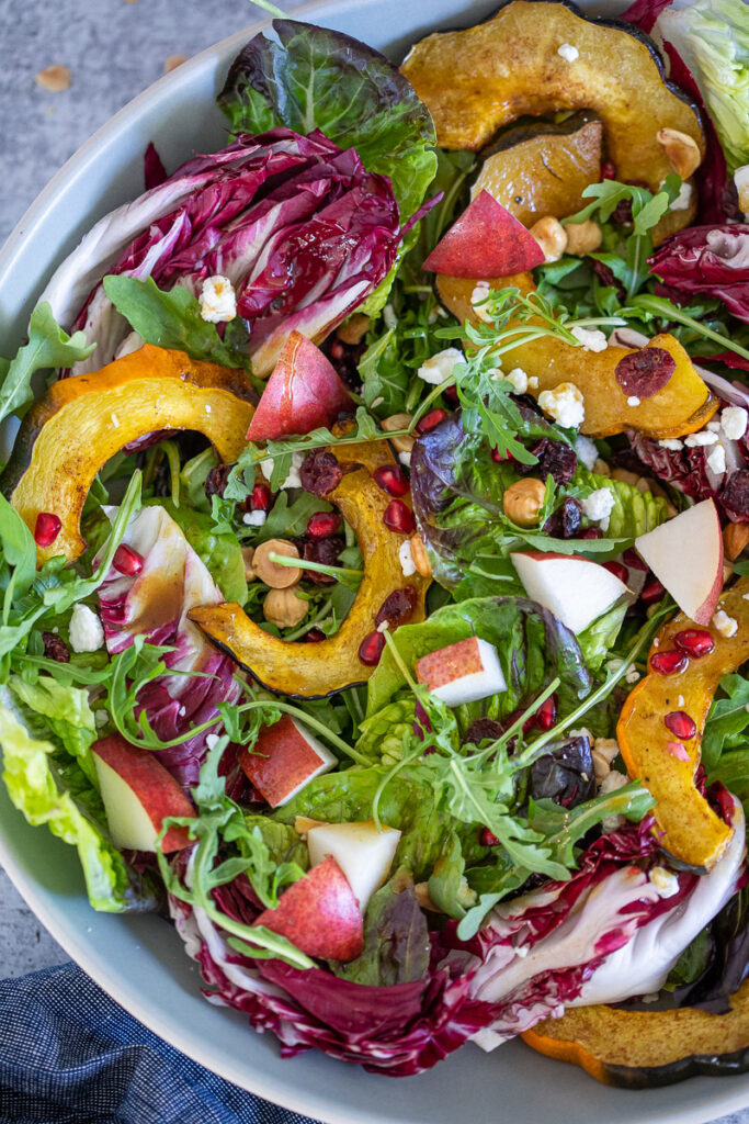 A bright Autuman Roasted Acorn Squash Salad with Maple-Spiced Vinaigrette boasting vivid colors of orange, reds and greens. 