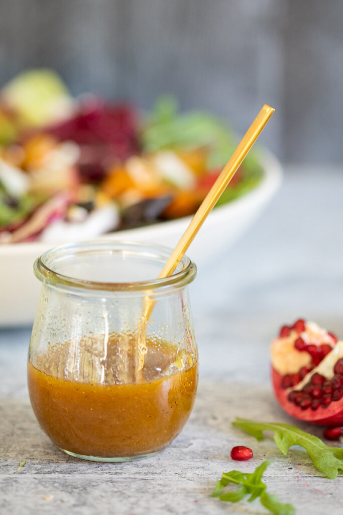 Maple-Spiced Vinaigrette in a small glass jar with a small gold colored serving spoon
